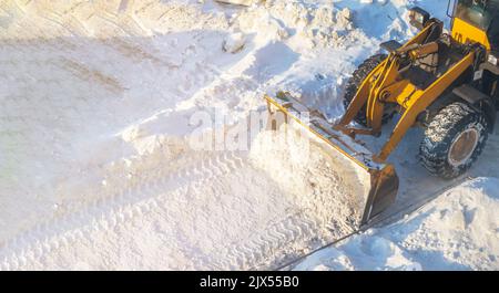 Un grande trattore arancione rimuove la neve dalla strada e libera il marciapiede. Pulizia e sgombero delle strade della città dalla neve in inverno. Rimozione della neve A. Foto Stock