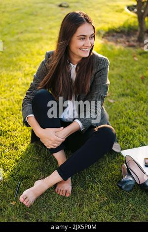 Giovane donna d'affari che riposa dopo una dura giornata, rilassandosi sul prato verde nel parco cittadino. Riposo estivo. Stagione estiva. Prendere pausa dal lavoro per l'equilibrio mentale Foto Stock