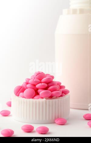 compresse o pillole rotonde rosa su sfondo bianco con bottiglia o contenitore, farmaci presi soft-focus con spazio di copia Foto Stock