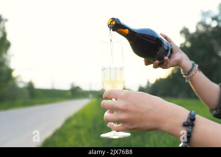Una donna versa lo champagne da una bottiglia in un bicchiere per strada. Vista frontale. Foto Stock