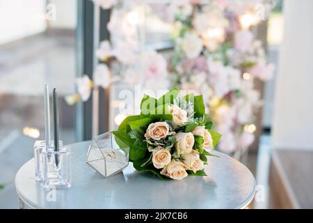 Un paio di splendidi anelli da sposa in un moderno piedistallo di vetro e un delicato bouquet di rose da sposa. Matrimonio, cerimonia. Messa a fuoco selettiva morbida. Foto Stock