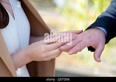 Sposarmi oggi e tutti i giorni, mani di una coppia eterosessuale di nozze. La sposa mise l'anello sul dito del marito. Messa a fuoco selettiva morbida. Foto Stock