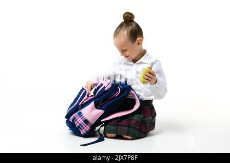 Ragazza carina in uniforme scuola raccoglie uno zaino per le classi isolato su uno sfondo bianco. Foto Stock