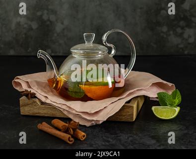 Tè rosso alla frutta con bacche in teiera di vetro su fondo nero. Foto Stock