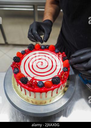 chef pof mano che prepara per glassa una torta di gocciolamento rossa nel laboratorio professionale della cucina Foto Stock