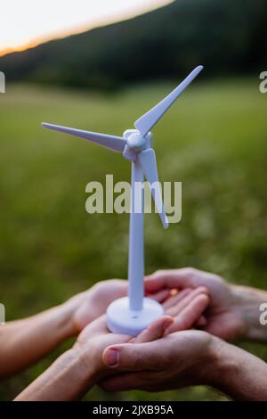 Primo piano di coppia in piedi in natura con il modello di turbina eolica. Concetto di futuro ecologico e di risorse rinnovabili. Foto Stock