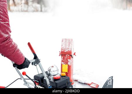 Primo piano di una soffiatrice portatile di neve rossa alimentata a benzina in azione. Uomo all'aperto che utilizza una macchina spazzaneve dopo una tempesta di neve per lo sgombero e la rimozione della neve su strade innevate. Rimozione della neve, assistente lanciatore Foto Stock