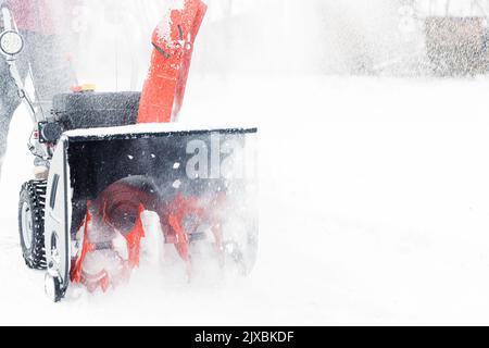 Dettaglio primo piano di una soffiante portatile da neve rossa alimentata a benzina in azione. Uomo all'aperto che utilizza una macchina spazzaneve dopo una tempesta di neve, nevicate per lo sgombero e la rimozione della neve. Rimozione della neve, assistente lanciatore Foto Stock