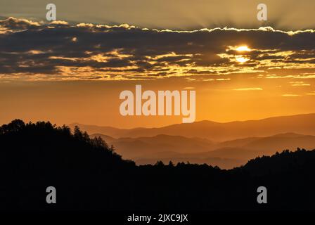 Paesaggio collinare di montagna silhouette con alberi di conifere all'alba. Sole nascosto dietro le nuvole. Bel cielo colorato. Raggi solari. Vrsatec Slovacchia Foto Stock