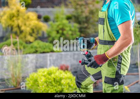 Primo piano del giardiniere caucasico che porta connettori e sprinkler nelle sue mani. Lavoro sull'installazione automatica del sistema di irrigazione del giardino per garantire la prop Foto Stock