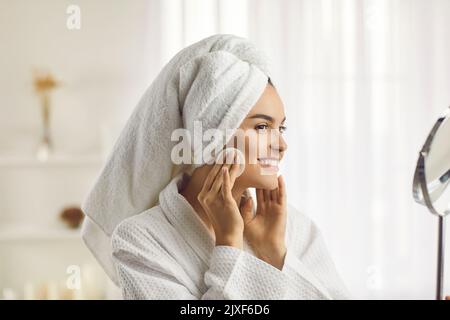 Giovane bella donna felicemente asciuga il suo make-up e pulisce il suo viso con un tampone di cotone rotondo bianco. Foto Stock