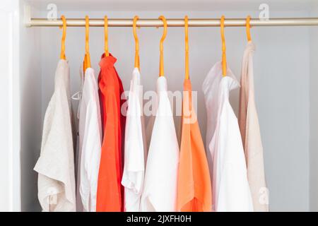 Abiti di colore corallo e bianco su grucce. Diverse bluse, camicie per un outfit casual. Sfondo del negozio di moda. Foto Stock