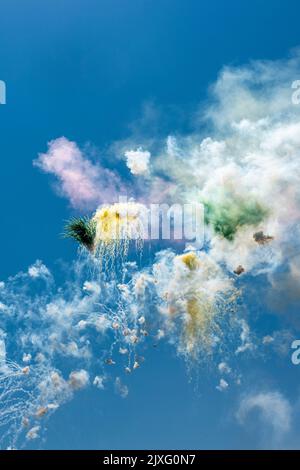 I fuochi d'artificio esplodono alla luce del sole contro un cielo blu segnano una festa religiosa in un villaggio siciliano Foto Stock