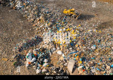 L'escavatore raccoglie i rifiuti da una discarica per il riciclaggio. Catastrofe ecologica dovuta a rifiuti non biodegradabili e plastica Foto Stock
