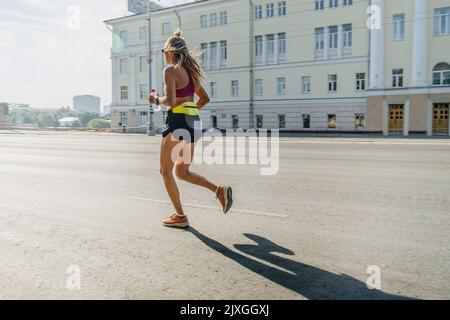 runner femminile che corre al mattino su strada cittadina Foto Stock