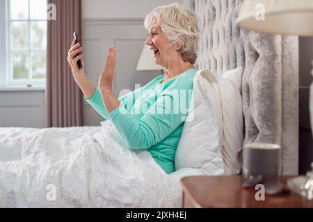 Donna anziana a casa con pigiama in letto fare videochiamata sul telefono cellulare Foto Stock