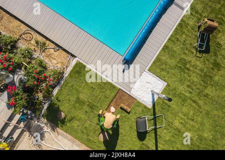 Vista aerea del paesaggista professionale caucasico finitura residenziale piscina paesaggio. Installazione di turfi e piantando alberi. Foto Stock