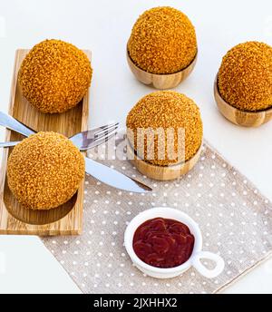 Deliziose uova scotch fatte in casa servite in ciotole di legno con salsa di pomodori e forchetta con primo piano di coltello sul tovagliolo Foto Stock