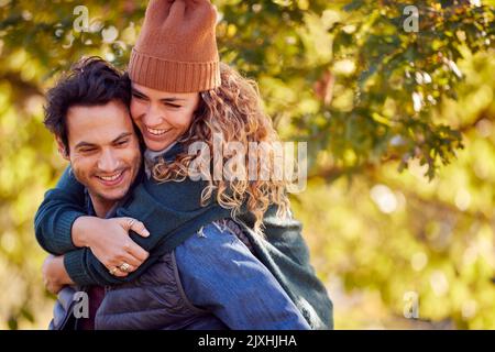 Felice coppia amorevole sorridendo come l'uomo dà la donna Piggyback nel Parco d'autunno Foto Stock