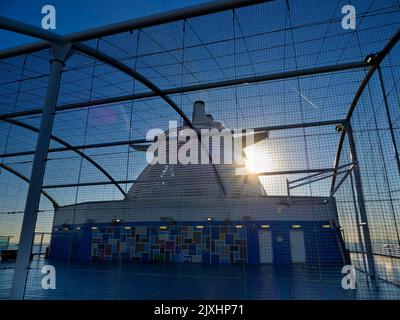 Guardando in alto dalla pista di una nave da crociera sul Mare del Nord, vediamo gli imbuti e la sovrastruttura della nave, attraverso le reti che circondano un bask Foto Stock