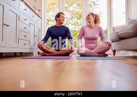 Coppia seduta sui tappetini a casa facendo esercizi di yoga insieme Foto Stock