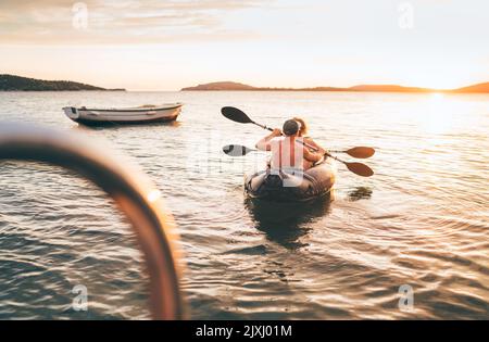 Due vogatori in kayak gonfiabili al tramonto di sera raggi mare Adriatico porto in Croazia vicino alla città di Sibenik. Vacanza, sport e ricreazione Foto Stock