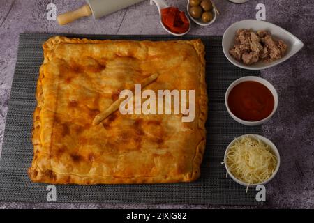 primo piano del ripieno di un'empanada di tonno con i suoi ingredienti su una tavola di legno con uno sfondo di mattoni Foto Stock