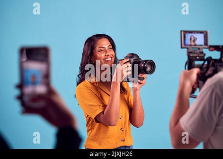 Donna matura in studio su Shoot con video e cellulare tenendo DSLR Foto Stock