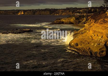 UN'ONDA CHE SI SCHIANTANO SULLA COSTA ROCCIOSA A LA JOLLA CON IL BELL'OCEANO PACIFICO BLU E CIELO NUVOLOSO A LA JOLLA CALFIORNIA Foto Stock