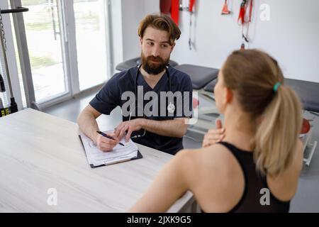 Donna atletica durante una consultazione in una clinica di riabilitazione lamenta di dolore al collo al suo medico fisioterapista Foto Stock