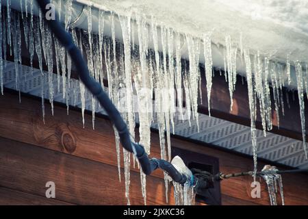 Ghiaccioli pericolosi sui cavi elettrici sotto il tetto della casa. Specifico per la stagione invernale Foto Stock