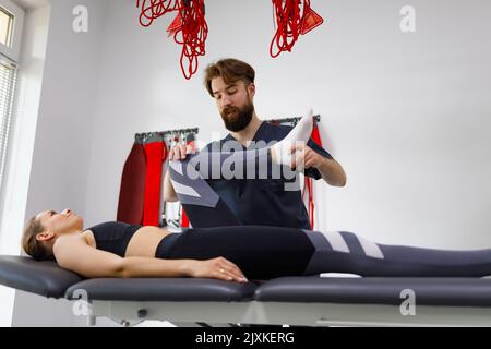 Uomo fisioterapista aiutare la donna con le gambe esercizi. Ginocchio del paziente flesso Foto Stock