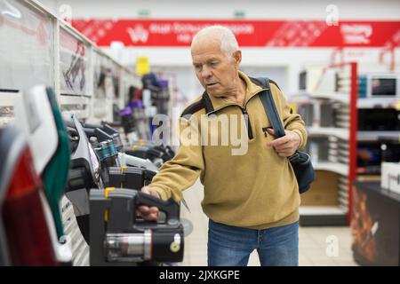 Uomo anziano che sceglie la felpa con cappuccio verticale nello showroom del negozio di elettrodomestici Foto Stock