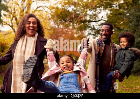 Sorridente Famiglia avere divertimento dondolante figlia a piedi attraverso la campagna contro gli alberi d'autunno Foto Stock