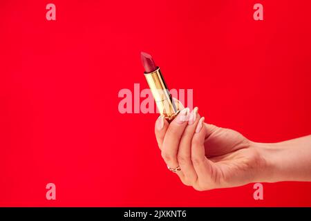 Primo piano Studio Shot di mano femmina Lipstick contro sfondo rosso Foto Stock