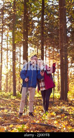 Una coppia matura in pensione cammina in autunno o in inverno nella campagna utilizzando la mappa o l'app di navigazione sul telefono cellulare Foto Stock