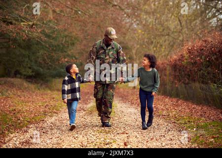 Soldato americano in uniforme ritorno a casa in congedo per la famiglia Holding mani con due bambini Foto Stock