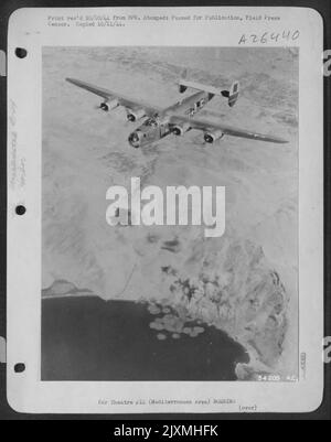 Sopra le installazioni del porto coperto di fumo a Scaramanga vola questo Consolidated B-24 Liberator del 15th AF il 24 settembre 44 come le sue bombe scoppiare sui pochi sommergibili rimanenti nel Mediterraneo e sulle strutture di comunicazione. I pesanti bombardieri Foto Stock