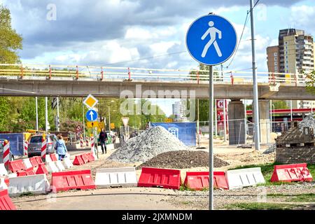 RIGA, LETTONIA - 13 MAGGIO 2022: Marciapiede pedonale in riparazione sulla strada Dzelzavas. Segnaletica stradale blu, blocchi rossi e bianchi in primo piano. Nuovo ponte in costruzione sullo sfondo. Foto Stock