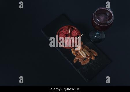 Primo piano di una tapa di chorizo in salsa, tipica salsiccia spagnola con pane e vino rosso estivo isolato su fondo nero Foto Stock