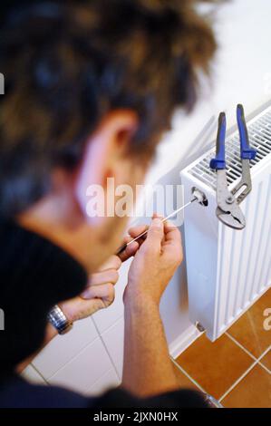 Uomo con cacciavite che fissa il radiatore. Primo piano di un apparecchio maschio di riparazione montato a parete. Lavoro su apparecchiature elettroniche con utensili a casa. Foto Stock
