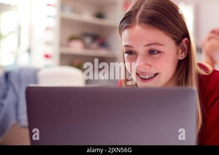 Ragazza adolescente che indossa pigiama utilizzando notebook sdraiato sul letto in camera da letto Foto Stock