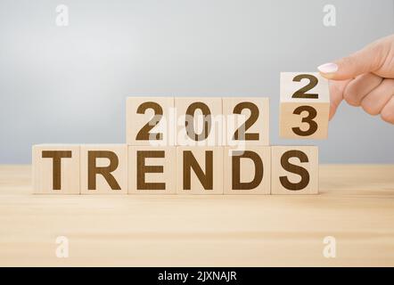 2023 concetto di tendenza. Mano flip cubo di legno cambiare anno 2022 a 2023. Sfondo grigio, copia spazio. 2022 concetto di tendenze. Cambia cubo di legno a mano Foto Stock