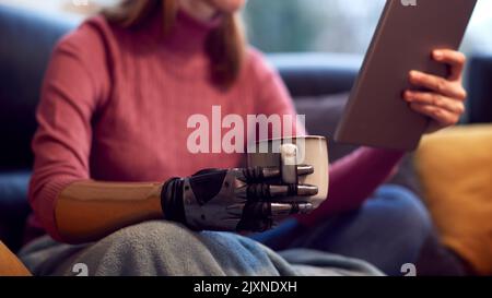 Primo piano della donna con braccio protesico e mano a casa utilizzando Digital Tablet bicchiere di caffè Foto Stock