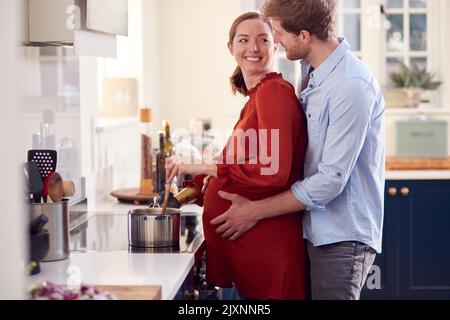 Coppia incinta con Donna con braccio protesico preparare il pasto in cucina insieme Foto Stock