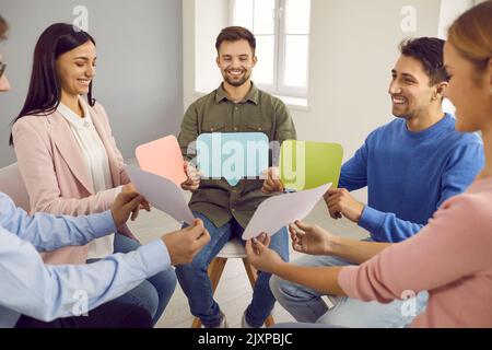Gruppo di persone felici con bolle di discorso che parlano durante una sessione di terapia di gruppo Foto Stock