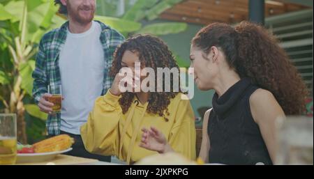 Un gruppo di amici si sta godendo un barbecue in un pomeriggio di sole. Tutti ridono e sono felici seduti al tavolo. Foto Stock