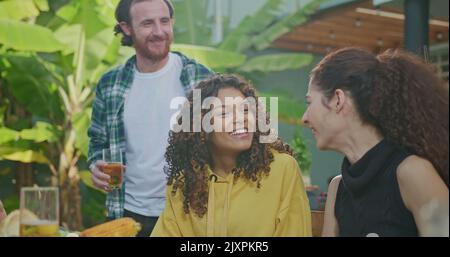 Un gruppo di amici si sta godendo un barbecue in un pomeriggio di sole. Tutti ridono e sono felici seduti al tavolo. Foto Stock