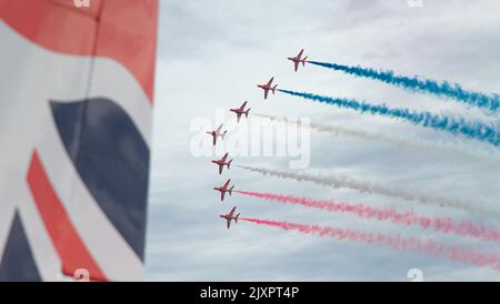 Royal Air Force Red Arrows Aerobatic Display Team volare in formazione con fumo rosso, bianco e blu con la coda di Una freccia rossa nel primo piano, B Foto Stock