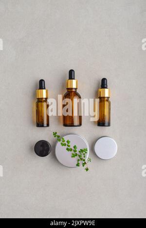 Bottiglie di vetro marrone contagocce, lattine cosmetiche in metallo e lattina di plastica piccola su fondo di cemento chiaro, vista dall'alto Foto Stock
